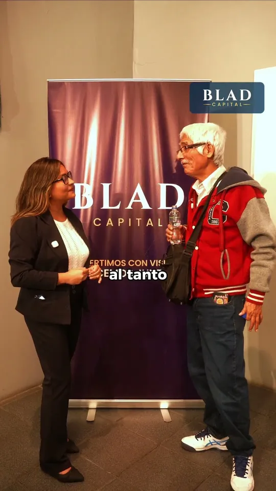 Testimonio 3: dos personas conversan de pie frente a un banner de BLAD CAPITAL.